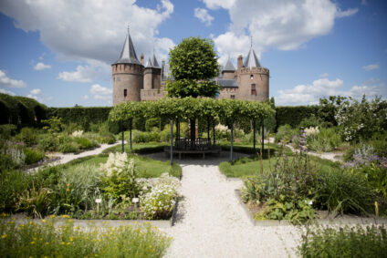 De Kruidhof van het Muiderslot staat in volle bloei. Het is zomer. Het kasteel staat op de achtergrond.