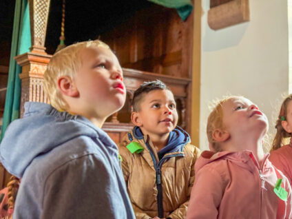 Drie kinderen luisteren naar hun museumdocent tijdens het educatieve programma Beestenboel. Ze dragen een fel groen naamkaartje.