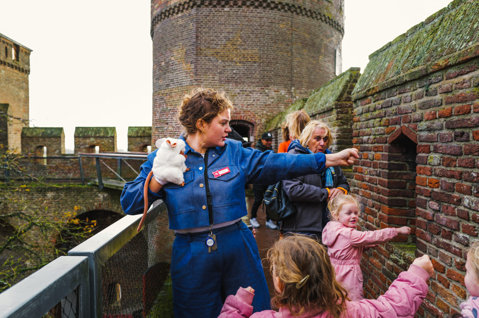 Twee kinderen krijgen les van een museumdocent. Ze staan op het kasteel met gebalde vuisten tegen de muur. De handpop, een grijze rat, doet mee.