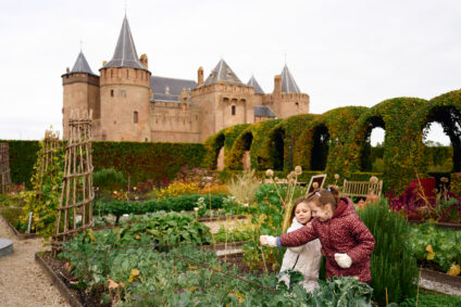 Twee kinderen lopen rond in de tuin op het Muiderslot. Het kasteel staat op de achtergrond. Het is koud buiten.