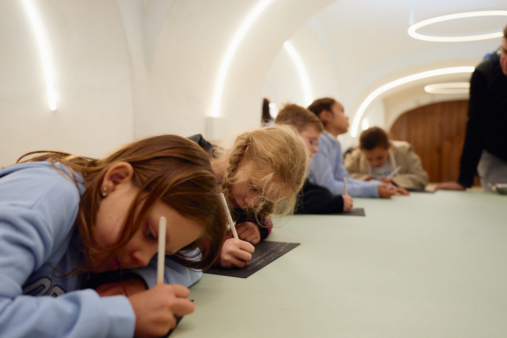 Kinderen zijn gefocust aan het schrijven met een wit potlood op zwart papier.