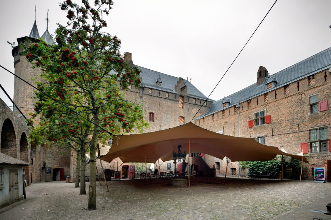 Een grote overkapping op het Slotplein vanaf de Zuidertoren. De overkapping is van zeil en wordt vastgehouden door draden en palen. De lucht is bewolkt.