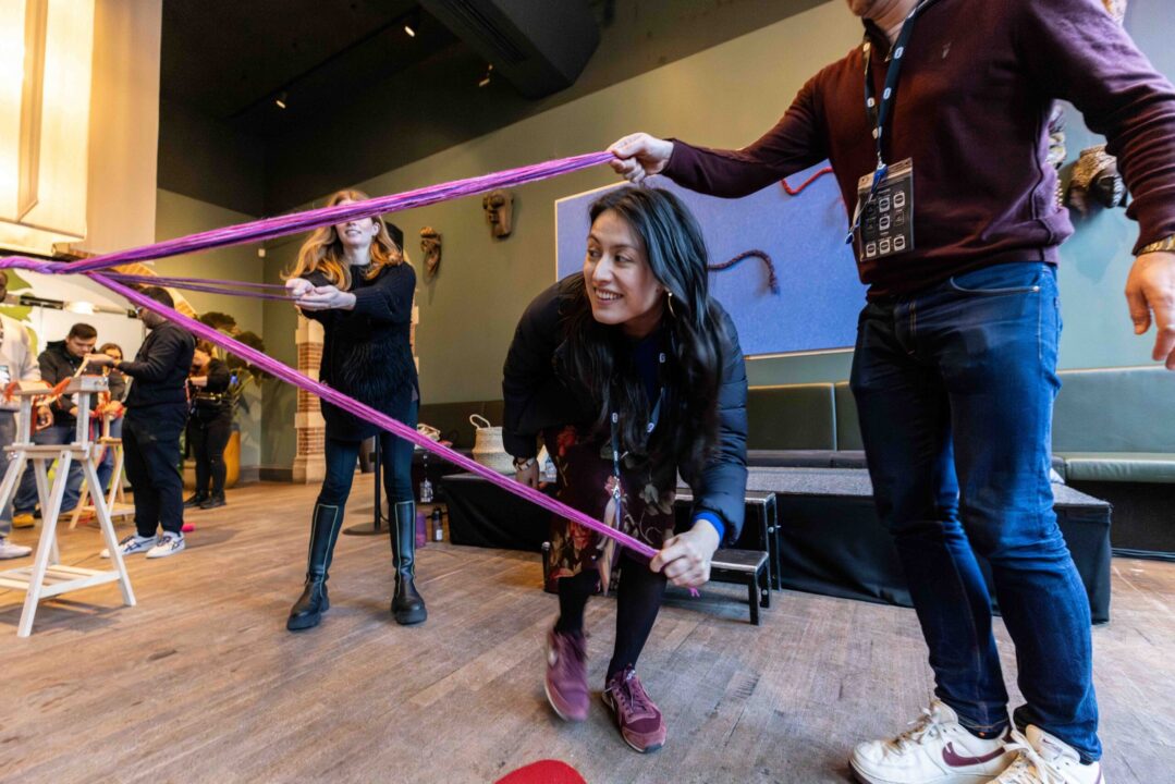 Een vrouw neemt deel aan de workshop 'In wol verweven'. Ze bukt en helpt met de creatie van een groot collectief textielkunstwerk. Het kunstwerk is paars.