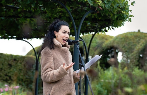 Spoken word artiest Soumaya Bazi staat achter een microfoon in de tuinen van het kasteel.