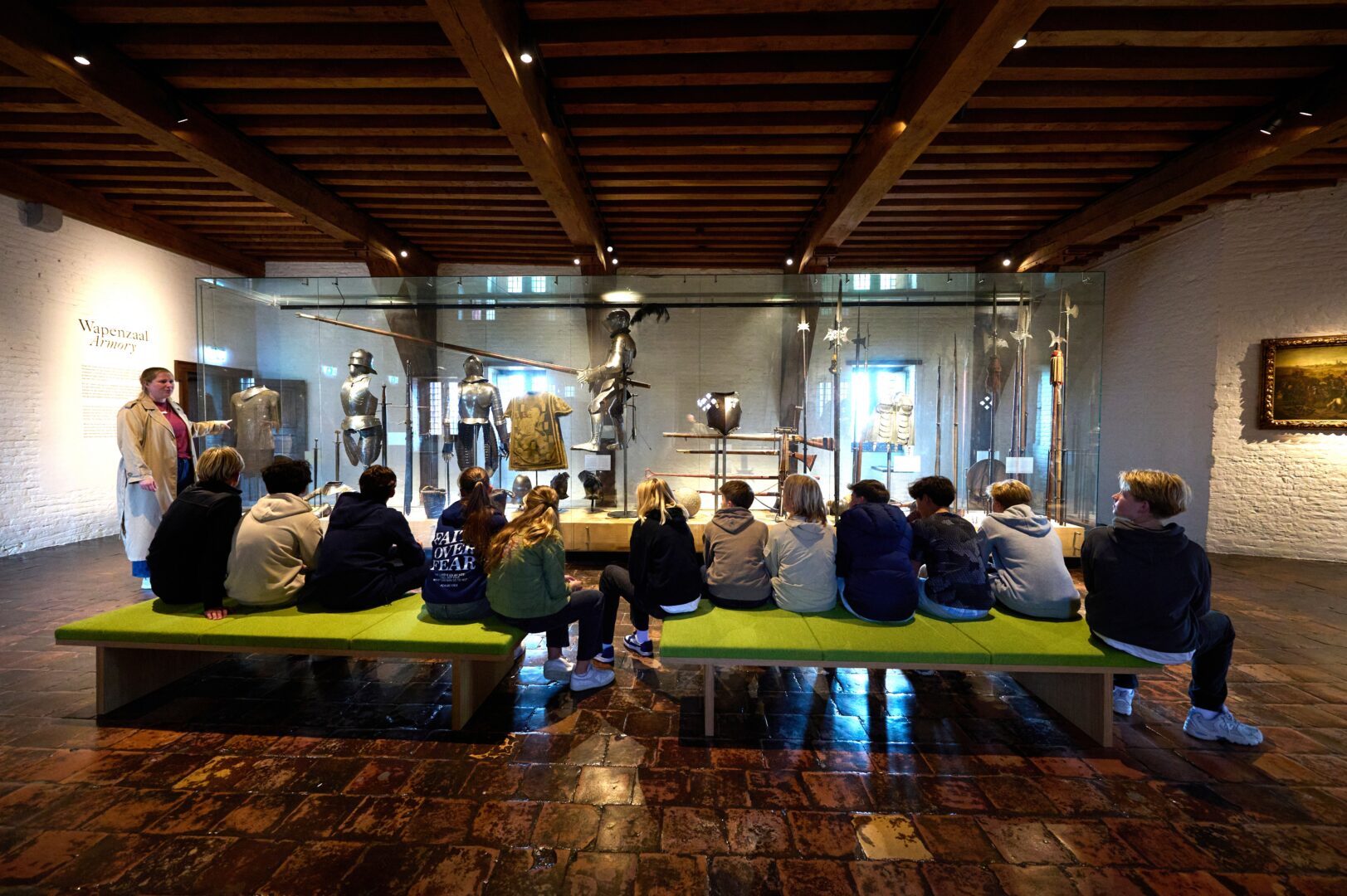 Een groep middelbare scholieren zit op bankjes en kijkt naar een presentatie van harnassen