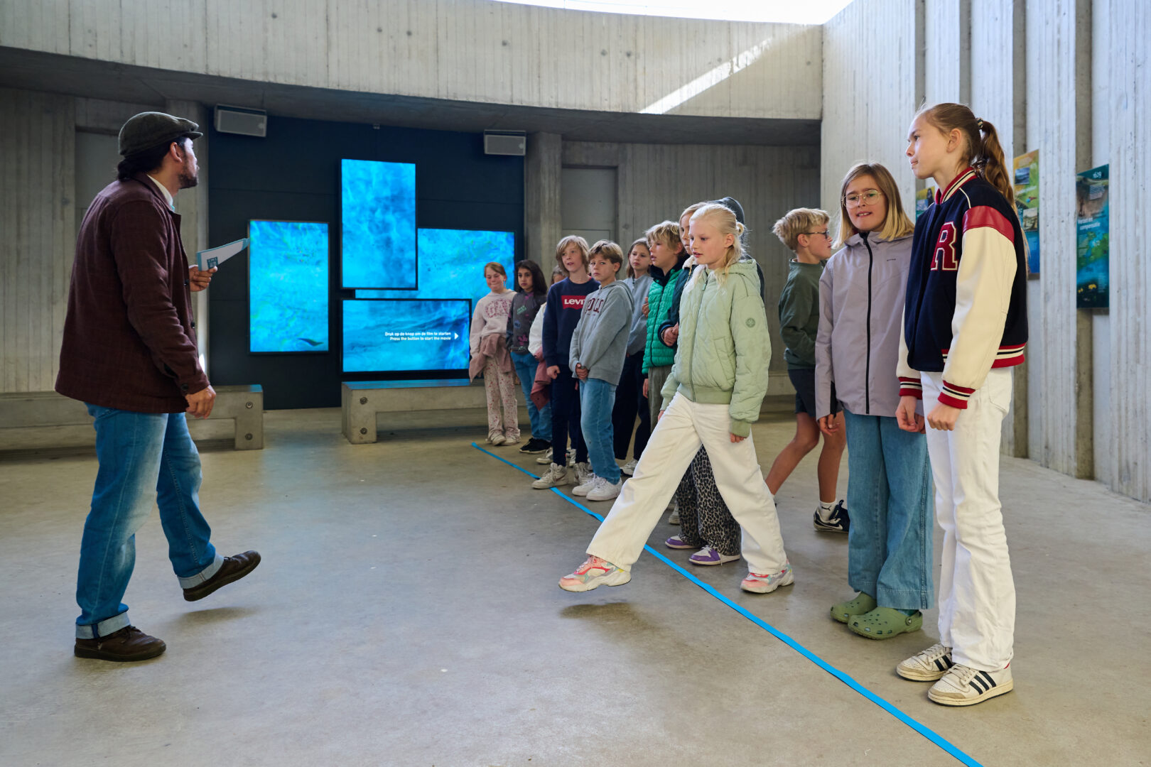 Een groep kinderen doet mee aan het educatieve programma Water: Vriend of Vijand? Ze luisteren naar de uitleg van Sefania Vitalis en spelen een spel.
