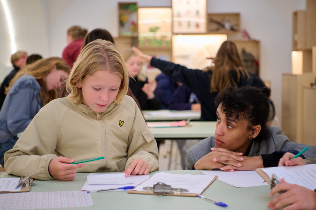 Een kind is opdrachten aan het maken tijdens het programma Oorlog en Vrijheid. Op de tafel ligt pen en papier.