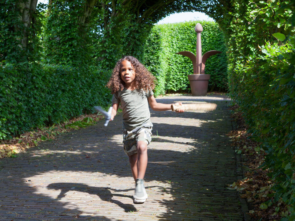 Een jongen rent met zwaard door de tuin.