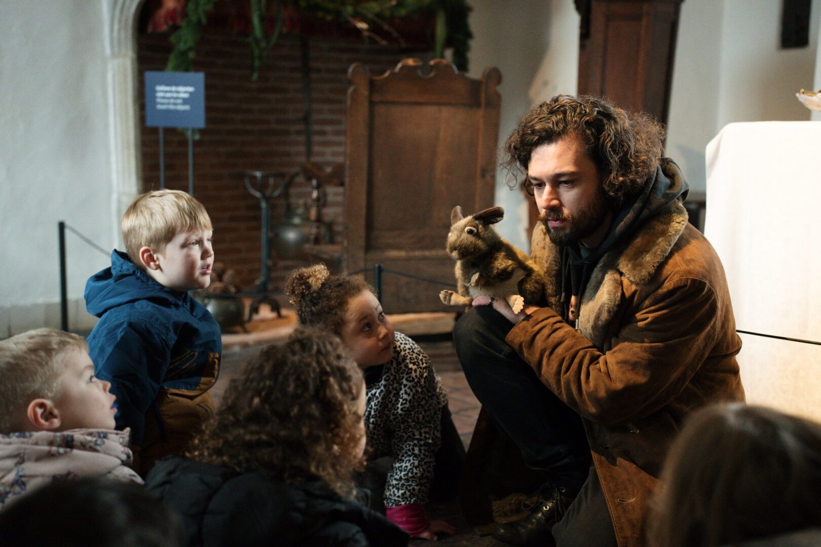 Een groep kinderen staan in het Muiderslot te luisteren naar een museumdocent met een handpop van een konijn. Het konijn is grijs met wit.