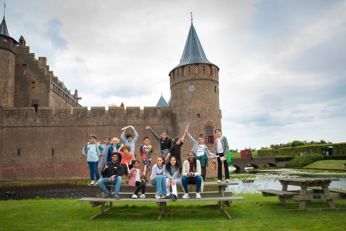 Kinderen staan op een picknicktafel voor het Muiderslot, in de zomer van 2020. Kinderen tussen 8 en 12 jaar oud deden mee aan een zomerschool samen met Fawaka Ondernemersschool.