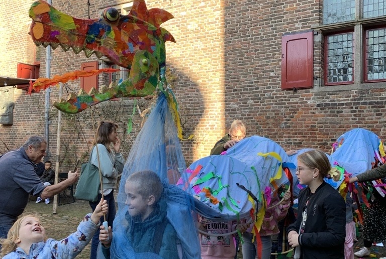 Kinderen lopen met een draak van stof over de binnenplaats van het kasteel Muiderslot