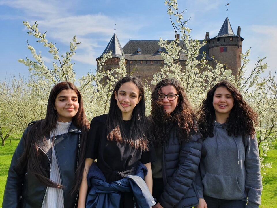 Vier scholieren poseren voor de pruimenboomgaard op het Muiderslot. Op de achtergrond is het kasteel te zien.