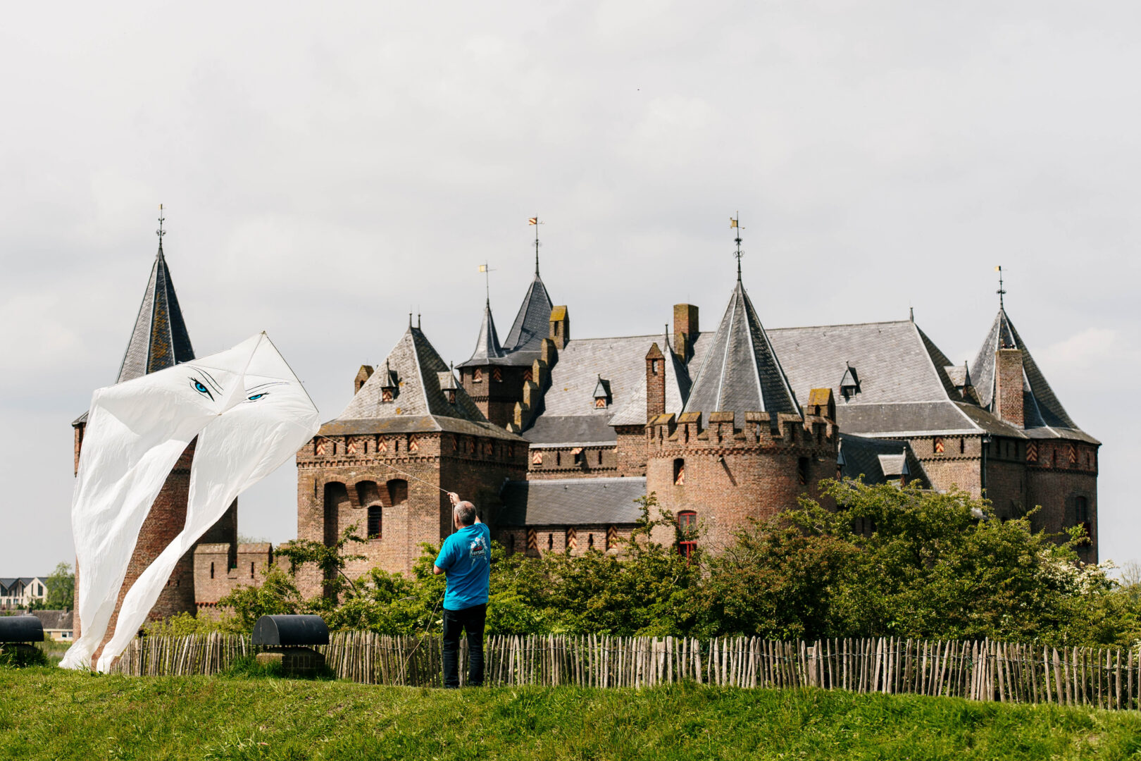 De zon schijnt in de tuinen van het Muiderslot. Een man is aan het vliegeren tijdens het vliegerfestival in mei 2024.