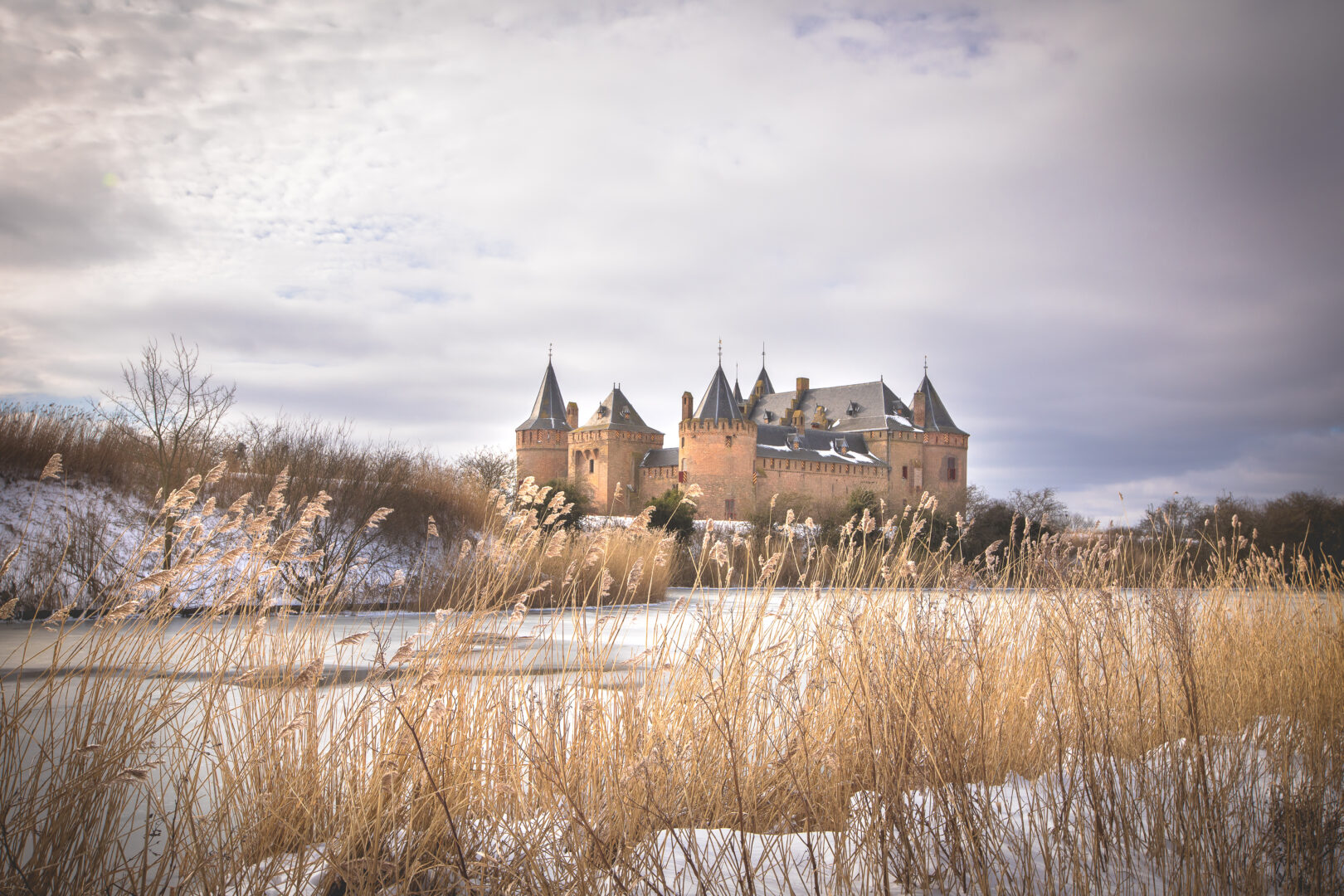 Het is winter, de lucht is bewolkt en het water is bevroren. Het Muiderslot ligt onder de sneeuw in februari 2021.