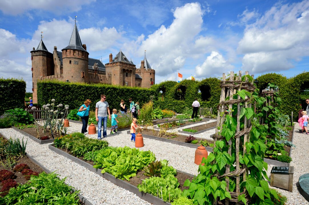 Mensen zijn aan het rondlopen op de Warmoeshof op het Muiderslot. De zon schijnt.