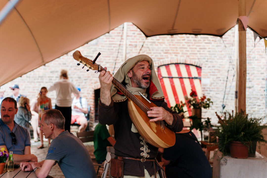 Een zingende man met middeleeuwse kleding en instrument loopt over de binnenplaats van het Muiderslot.