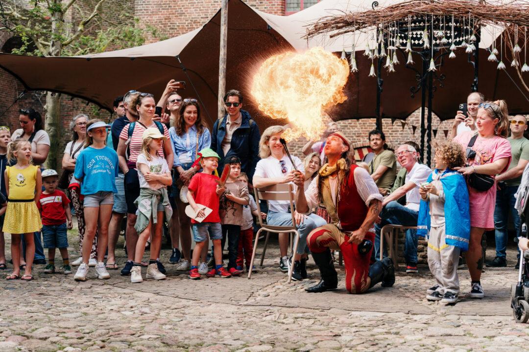 A large crowd watches an artist in medieval clothing in the courtyard of the Muiderslot.