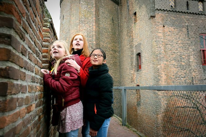 Vier kinderen zijn op schoolbezoek op het Muiderslot. Ze kijken uit de schietramen van het kasteel.