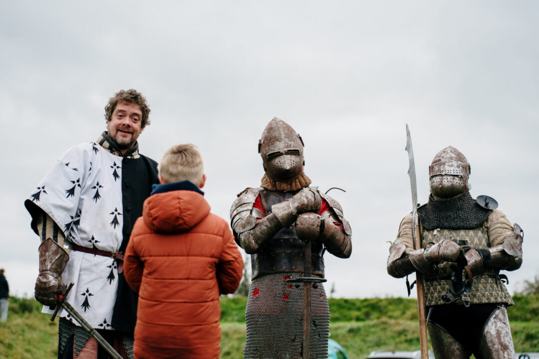 Een kind kijkt naar drie volwassenen die als ridder en in harnas zijn verkleed.