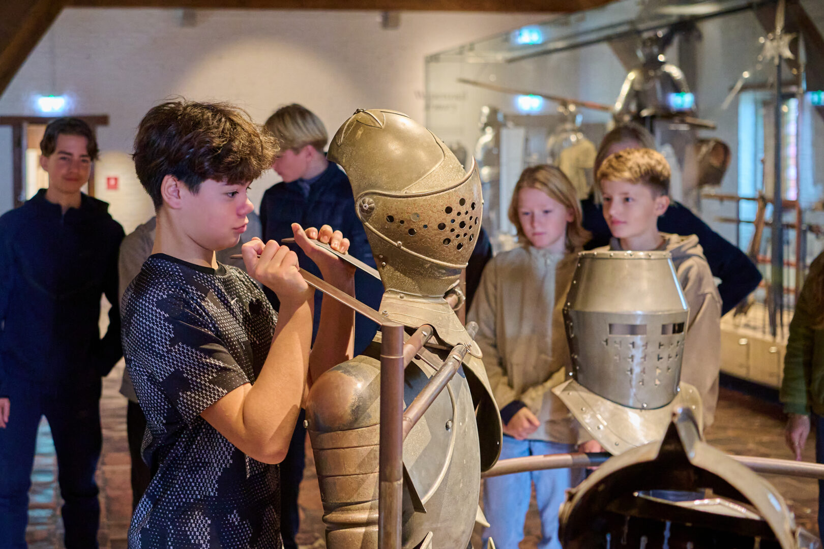 Boy lifts a suit of armor to feel how heavy it is during an interactive tour of the Muiderslot.