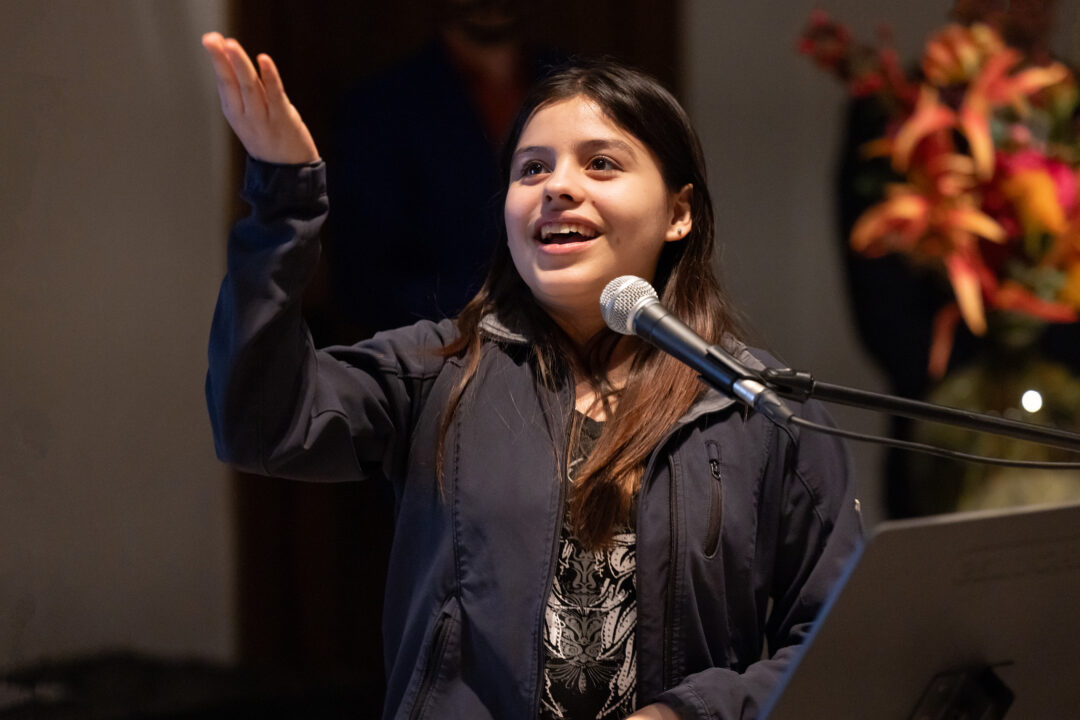Young girl stands at a microphone and holds a lecture.