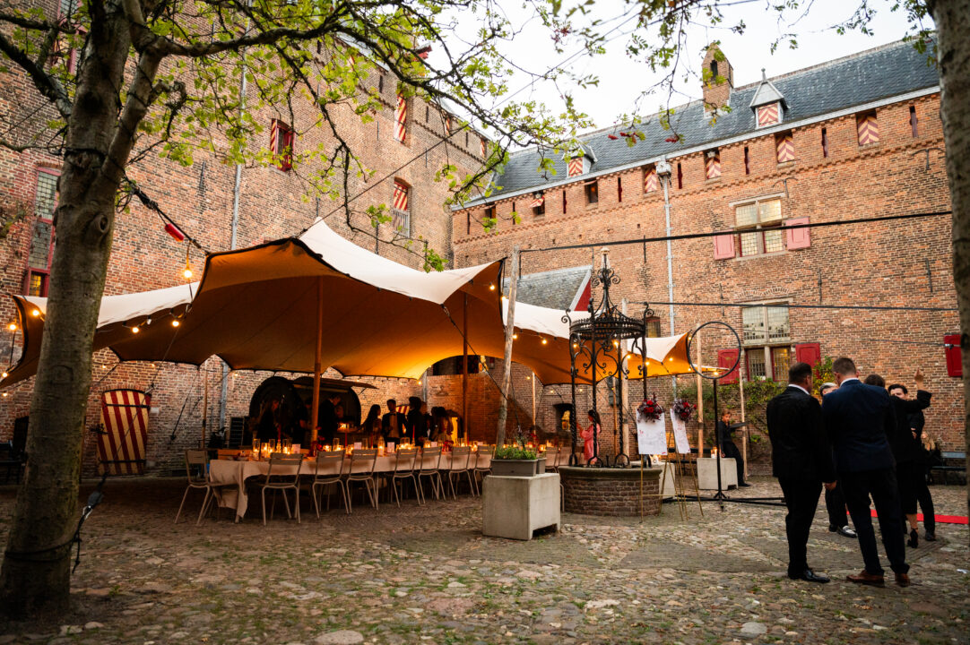 Binnenplaats kasteel met onder een overkapping gedekte tafels met kaarslicht.