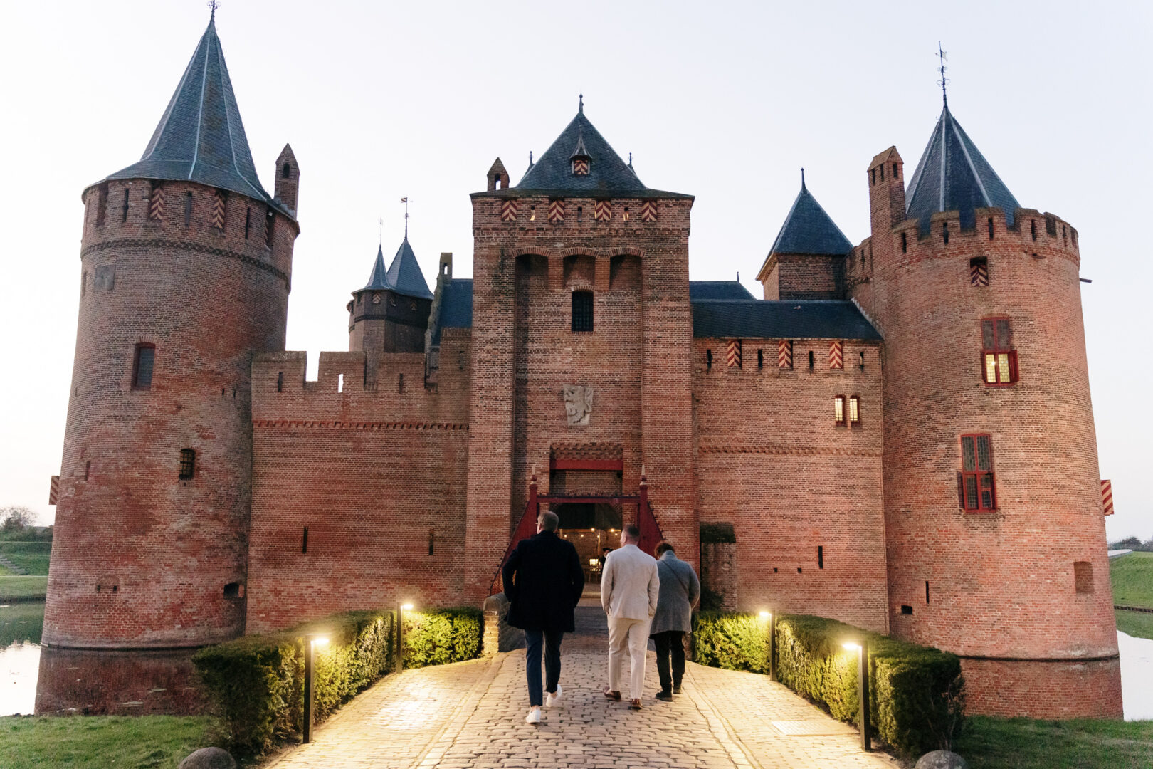 Drie mannen in pak lopen richting de kasteelpoort.