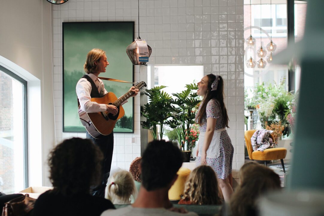 Man met gitaar speelt en vrouw staat erbij en zingt tijdens een voorstelling.