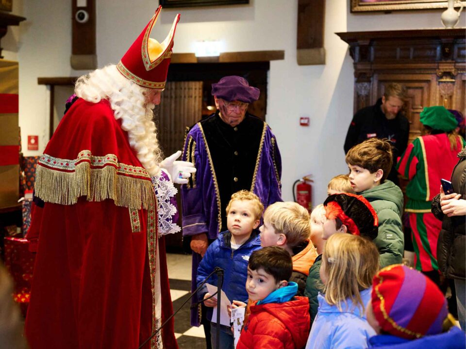 Sinterklaas begroeten kleine kinderen in de ridderzaal en is in gesprek met ze